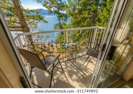 Light hotel balcony with view on pine forest and mountain lake. Chair, table, two wine glasses.