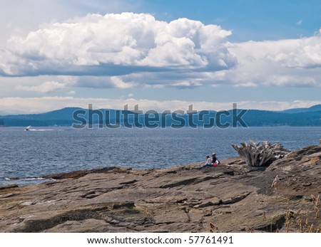 A family sitting on a seashore rocks and watching the boat at the sea.