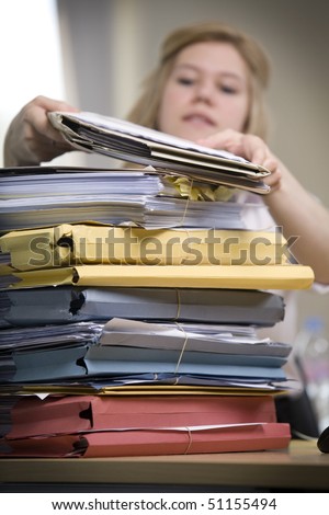 An attractive office worker slowly gets through a large stack of files.