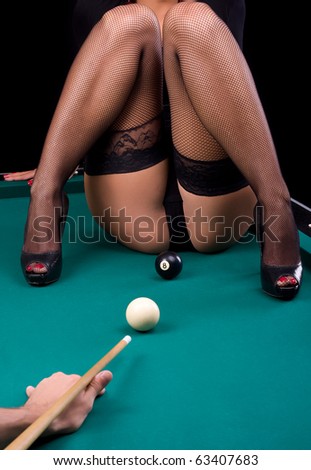 Studio shot of woman sitting on pool table, eight ball and pool cue.