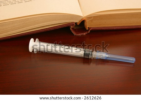 Syringe on desk with an open research book.
