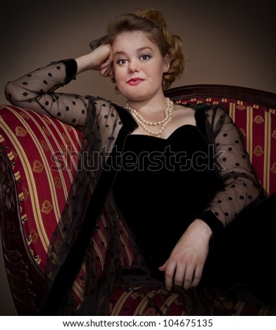 Vintage style portrait in the victorian style seated on a couch in vintage dress.