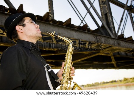 A saxophonist plays outdoors at sunset against a grungy industrial skyline.