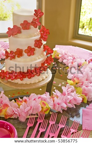 A wedding cake with red flowers surrounded  by pink flowers.