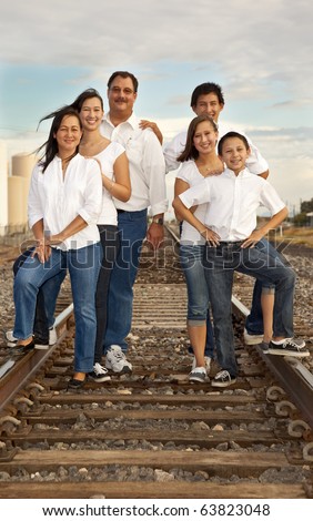 A multicultural family of six photographed at  sunset in an industrial location featuring railroad  tracks.