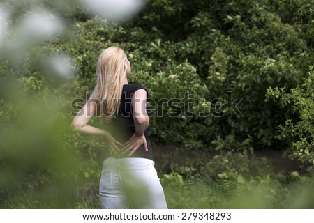 Back Pain. Back view of woman rubbing the muscles of her lower back over a nature background.