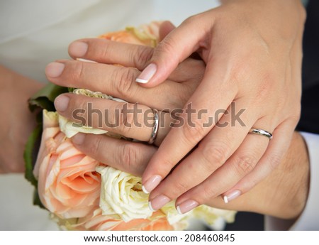 bride and groom hands with White gold rigs on the wedding bouquet background