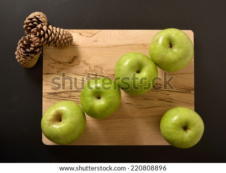 green apples and pine cones on wooden chopping board isolated on black abstract background