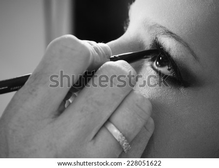 Make up artist drawing an eye line with a pencil on a model close up in black and white