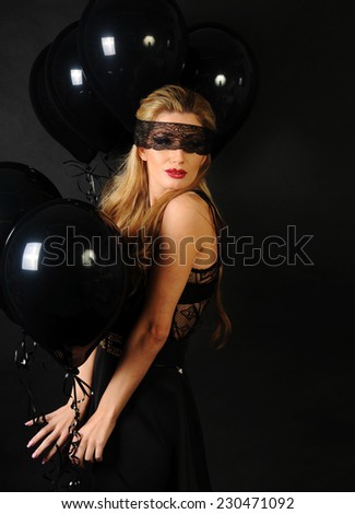 Young beautiful slim girl wearing black lace sensual top and black skirt with evening make up and black lace band on her eyes posing with black balloons on black background