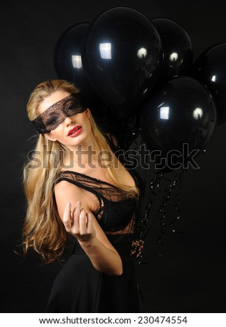 Young beautiful slim girl wearing black lace sensual top and black skirt with evening make up and black lace band on her eyes posing and playing with black balloons on black background