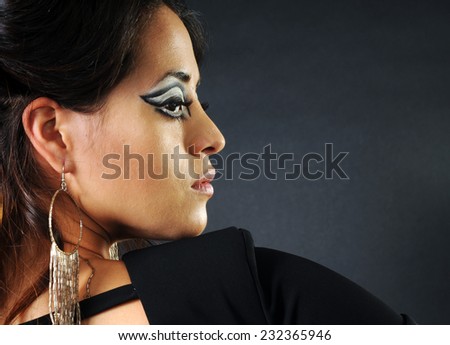 close up profile portrait of Young latin woman wearing long earrings and scenic make up isolated on black