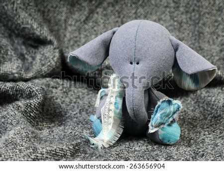handcrafted beautiful sad baby elephant interior toy holding a blue heart made of all natural materials on grey background