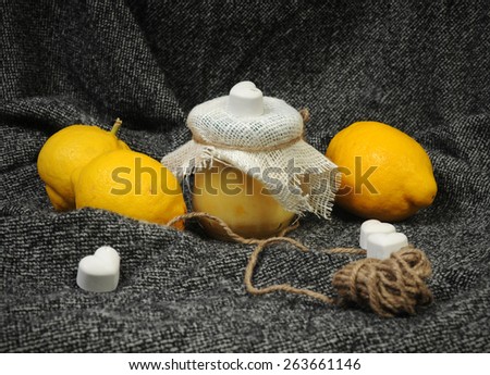 still life with a lemon curd jar and bright yellow lemons decorated with chalk hearts and linen on grey background