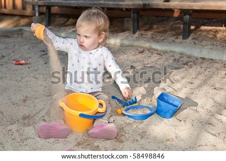 Cute Caucasian baby girl playing with the sand in sandpit.