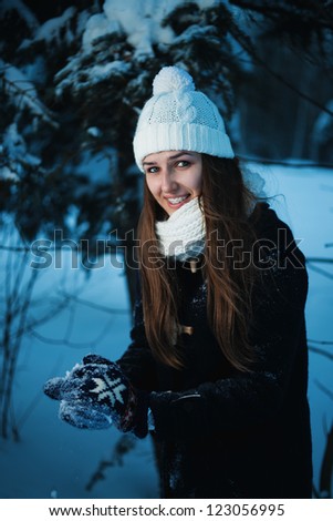 Smiling woman with braces on her teeth holding snowball outdoors in the evening sun