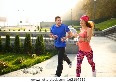 Young couple of athletes running on the empty street in the morning. The man is looking at his partner. Everyone is smiling.