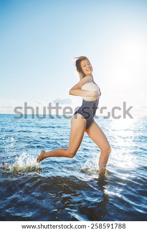 Young woman running in the water with volleyball against horizon line