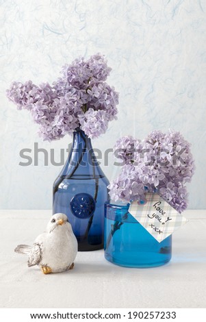 Still life with Lilacs in blue vases, a little bird and a card with the words: Love you