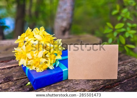 Bouquet of flowers Narcissuses on natural wood background with gift. Nature light.