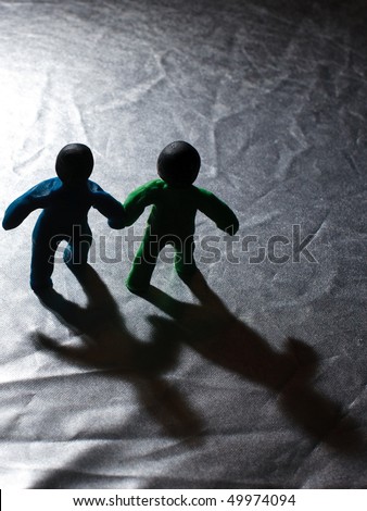 Two abstract (green and blue) of clay man holding hands with a shadow in the void.