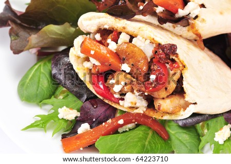Pitta bread on salad leaves filled with a chicken, vegetables and feta cheese