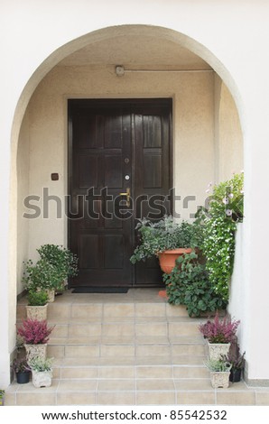 Porch with a wooden dark brown door and flowers