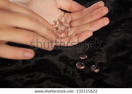A woman with fake diamonds in her hand counting them out on a black velvet tabletop