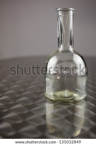 Empty glass bottle on a polished stainless steel table against a dark grey background