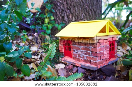 Hand built garden decoration of a house for gnomes and fairies against a large tree between ferns, rocks and leaves