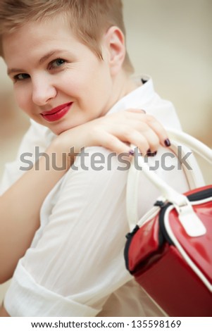 Beautiful caucasian female fashion model wearing a white blouse and black skirt against a neutral background, carrying a red handbag
