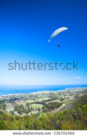 Paraglider launching from the ridge with a yellow and white canopy. The shot is taken right after takeoff. The canopy wingtip is sharp, with slight movement on the closer wing and the pilot