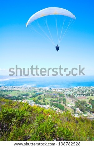 Paraglider launching from the ridge with a yellow and white canopy. The shot is taken right after takeoff. The canopy wingtip is sharp, with slight movement on the closer wing and the pilot