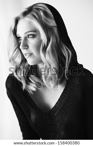 Sexy and beautiful young adult caucasian woman in black lingerie and a knitted see through hoodie in a light white bedroom