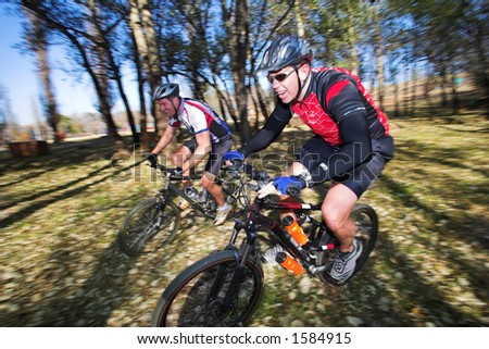 Panning shot of two mountain bikers, racing in a forest.  Movement, some of the bikers in focus.