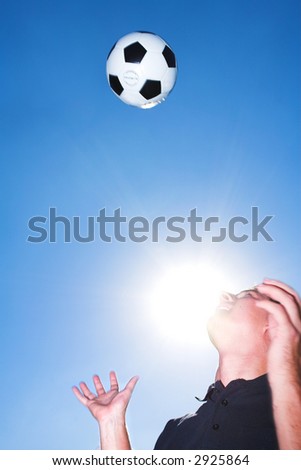 A male soccer referee or coach catching a soccer ball. The sun is shining from behind his face. There is movement on his hands and the ball but elements of the face is sharp.