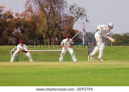 Cricketers playing in the late afternoon, Batsman hitting ball, fielder running forward on green cricket pitch - Overcast Day, before the storm - EDITORIAL USE ONLY