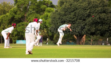 Cricketers playing in the late afternoon, Bowler bowling ball, fielder running forward on green cricket pitch - Overcast Day, before the storm. movement on bowler, focus on batter. Editorial use only