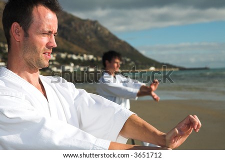 Young adult men with black belt practicing a Kata on the beach on a sunny day (person in background hidden)