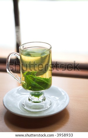 Hot green mint tea standing next to a window with whole mint leaves (shallow Depth of Field)