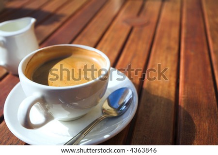 A cup of coffee on a wooden table in an outdoor cafe. Shallow depth of field, focus on the rim of the cup