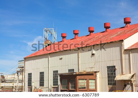 Corrugated iron building with red roof on mine premises with shaft winch in the background. Blue sky and sunny day