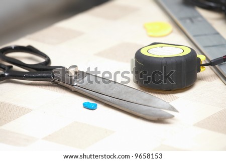Industrial sewing room tools, lying on a table, including a pair of scissors, marking chalk, ruler and measuring tape (Shallow Depth of Field ? focus on measuring tape)