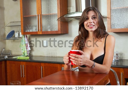 Sexy young adult brunette woman in black lingerie eating breakfast and drinking coffee in her kitchen