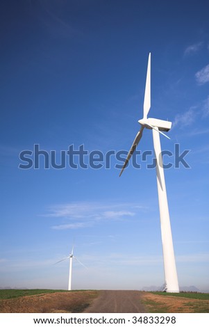 Wind powered electricity generators standing against the blue sky in a green field on the wind farm