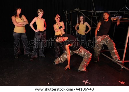 A group of female and one male freestyle hip-hop dancers during dance training session on stage. Lit with spotlights