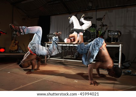 Three Freestyle hip-hop dancers in a dancing practice session on stage with instruments. Lit with spotlights. Movement on edges of dancers