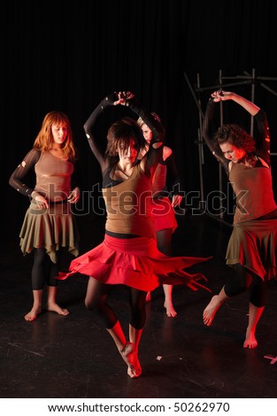 A group of four female freestyle hip-hop dancers in a dancing training session. Lit with spotlights. Movement on edges of dancers