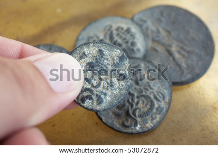 A man  holding antique ancient Greco-Roman coins from Turkey, on a smooth leather sheet background.