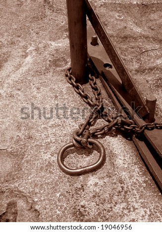 Rusty chain with shackle around a steel pole on a granite stone ground